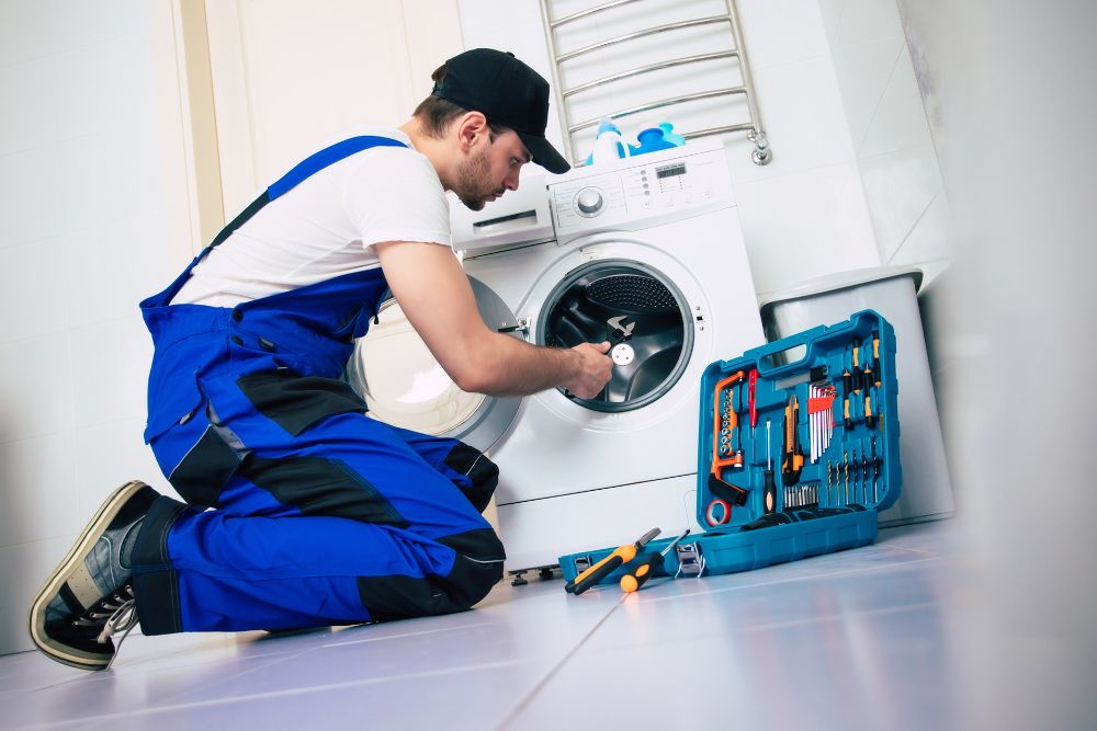 A man wearing overalls works on a washing machine, highlighting appliance repair services available in Miami, FL.