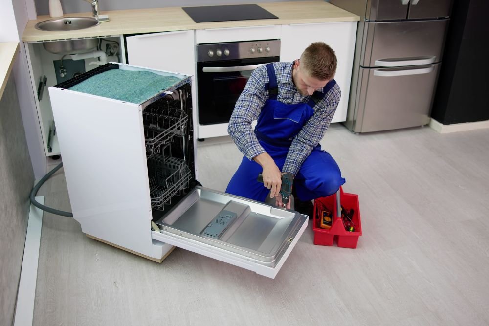 A man in overalls is engaged in repairing a dishwasher, showcasing kitchen appliance repair in Miami, FL.