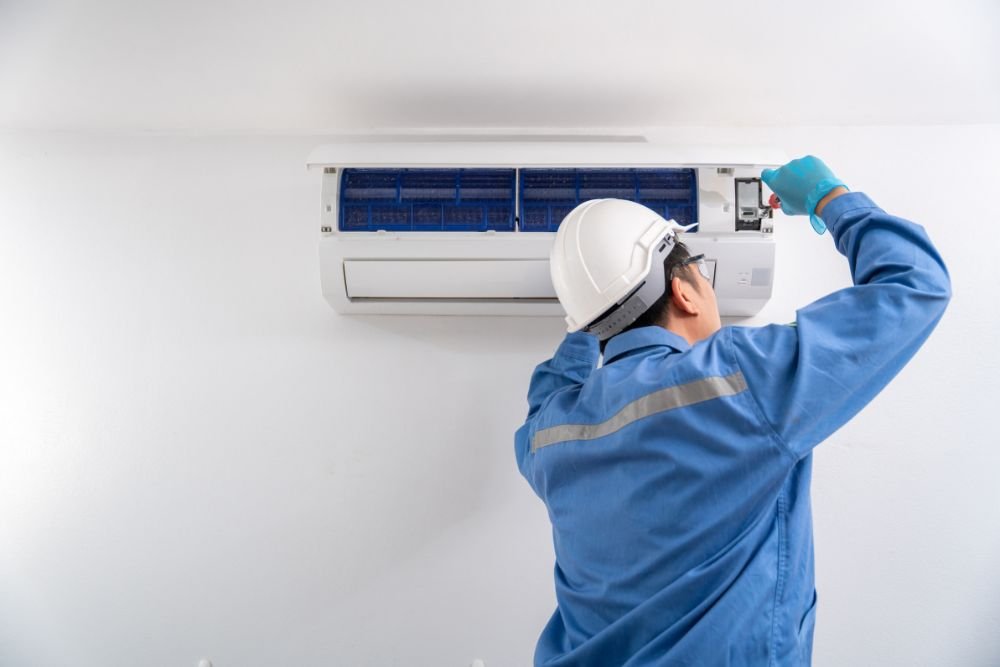 A man wearing a hard hat and blue overalls fixes an air conditioner, showcasing HVAC repair services in Miami, FL.