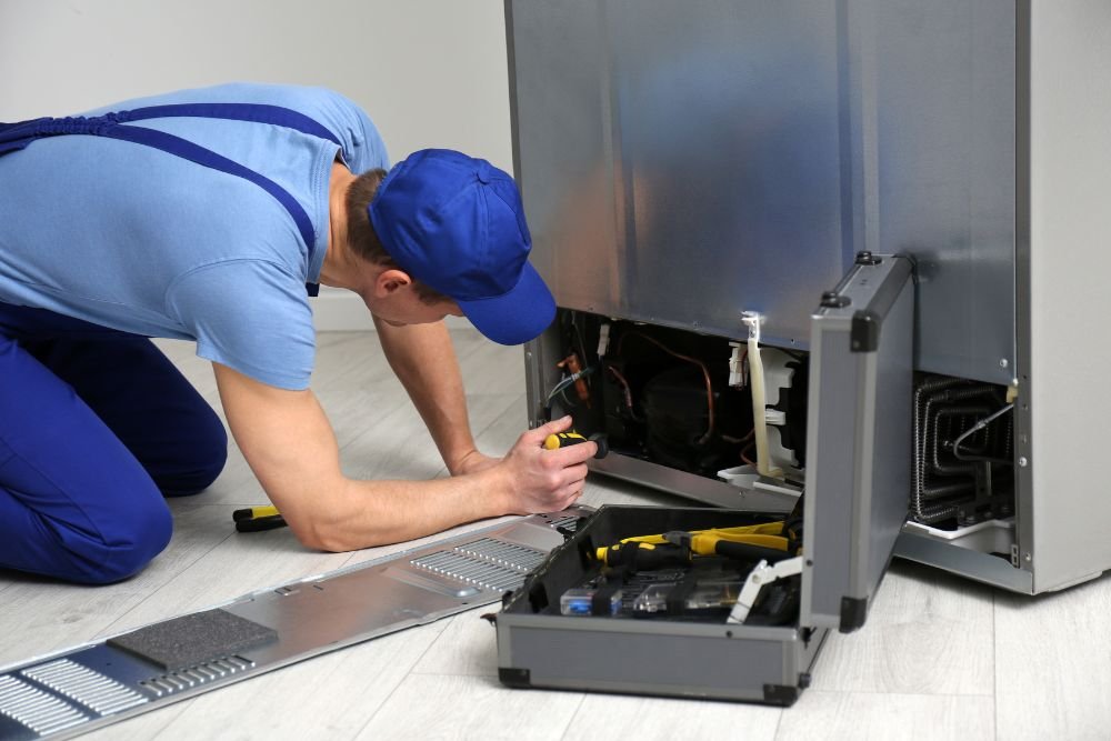 A man wearing overalls is fixing a refrigerator, showcasing commercial appliance repair services in Miami, FL.
